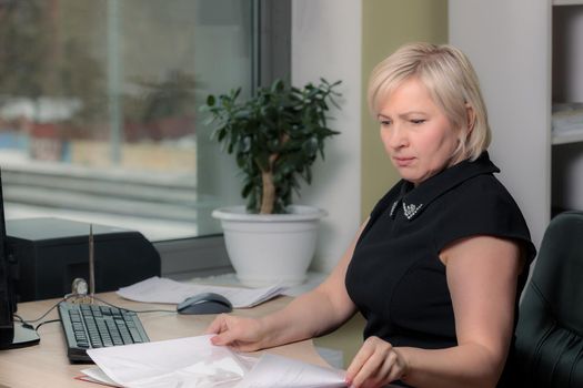 A female director working in an office is sitting at a table, analyzing business statistics, checking documents. Close-up.