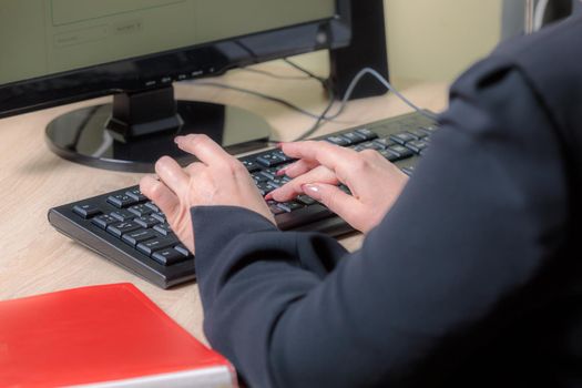 A woman director working in an office is sitting at a table, typing on a keyboard, checking documents. Close-up.