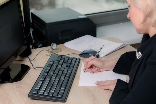 A female director working in an office is sitting at a table, analyzing business statistics, checking documents. Close-up.