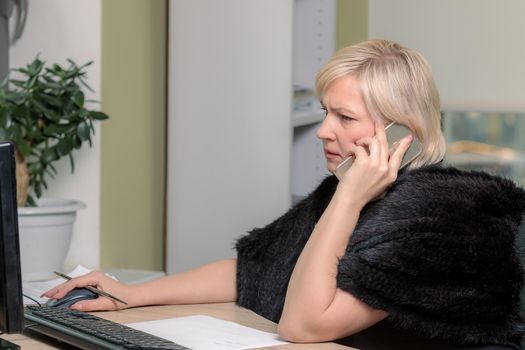 A woman director working in an office is sitting at a table, talking on the phone, checking documents. Close-up.