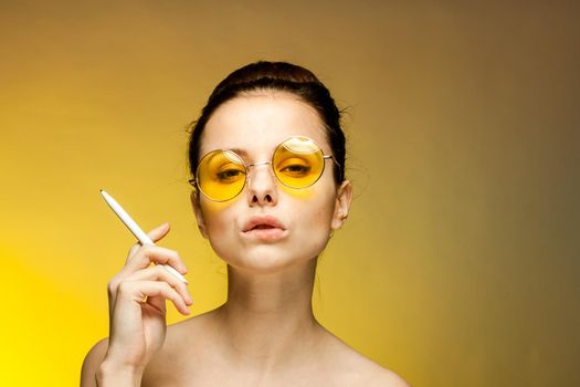 brunette in yellow glasses naked shoulders cigarette in hands emotions yellow background. High quality photo
