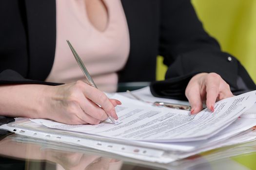 A woman director working in the office sits at the table, signs documents. Close-up.