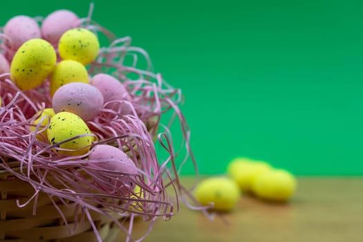 Colorful Yellow and Pink easter egg with freckle patterns on wooden table with copy space. Pink and Yellow easter egg inside a basket
