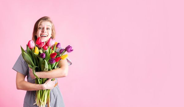 Women's Day or Mother's Day celebration. Banner. Happy young woman holding bouquet of fresh tulips isolated on pink background