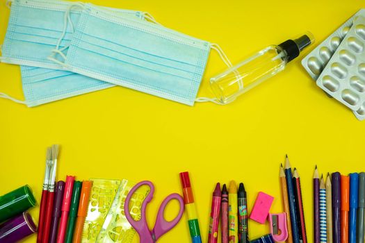 School supplies like pencil scissor eraser ruler watercolor mask alcohol sanitizer on yellow background. Back to school concept during covid pandemic with copy space