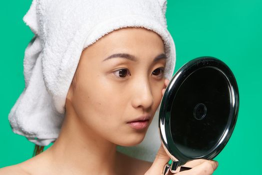 woman of asian appearance looks in the mirror with a towel on her head clean skin. High quality photo