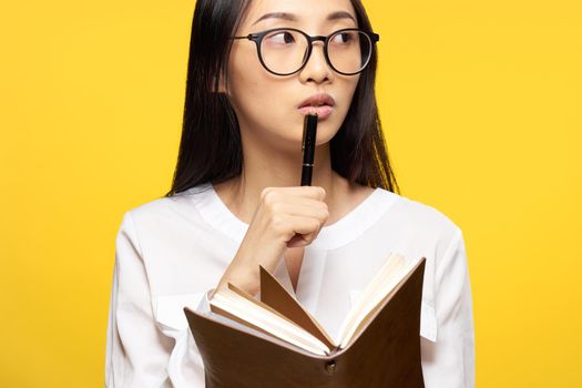 Business woman with a notebook in her hands holds a pen near her lips elegant style yellow background. High quality photo