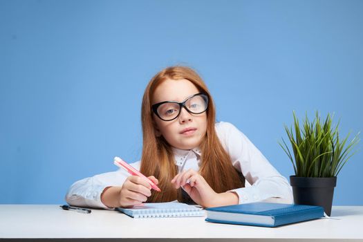 red-haired girl with glasses doing homework at the table school education. High quality photo