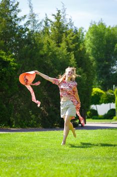 A charming girl in a light summer sundress and a pareo hat is walking in a green park. Enjoys warm sunny summer days.