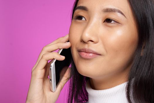 woman of asian appearance with a phone in hand communication close-up pink background. High quality photo