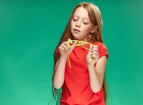 girl with red hair holding yellow glasses in her hands green background studio red t-shirt. High quality photo