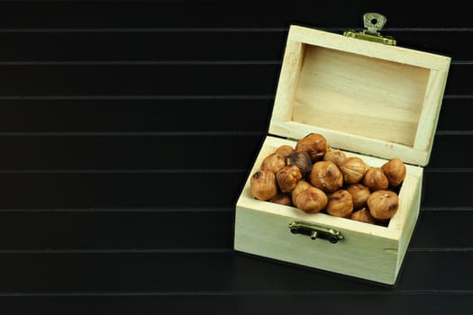 Nuts, hazelnuts peeled in a wooden box. Hazelnut kernels in a wooden chest, close-up on a black background.