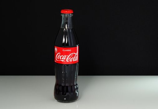 Coca cola, a classic glass bottle with a logo and red lid, is insulated on a black-and-white glass background. High quality . Russia, Nizhny Novgorod, 20.02.2021 