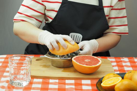 A young woman makes freshly squeezed juice from oranges and grapefruit on a hand-made juicer. High quality photo