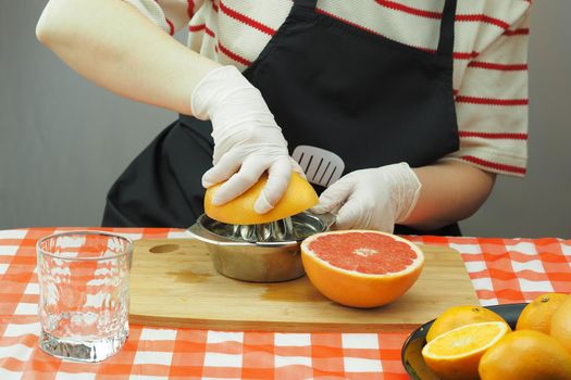 A young woman makes freshly squeezed juice from oranges and grapefruit on a hand-made juicer. High quality photo