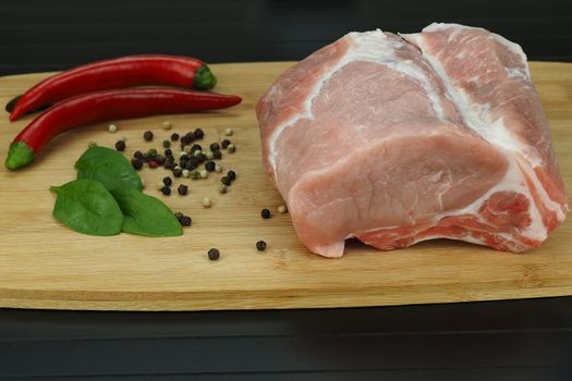 A piece of raw meat with pepper pods, peas and coarse salt on a wooden board.