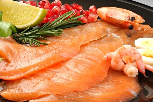 Appetizing slices of sliced salmon with lemon shrimp and pomegranate on a black plate, delicious food. High quality photo