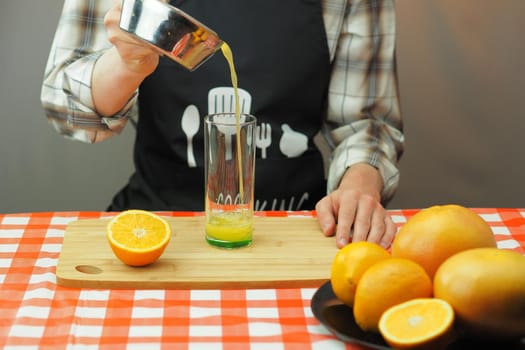 A young man pours freshly squeezed citrus juice into a transparent glass. High quality photo