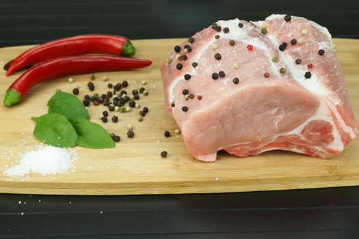 A piece of raw meat with pepper pods, peas and coarse salt on a wooden board.