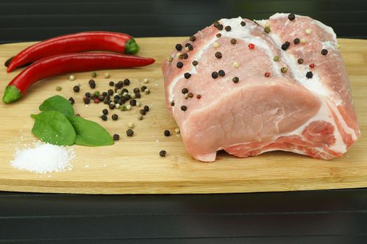 A piece of raw meat with pepper pods, peas and coarse salt on a wooden board.