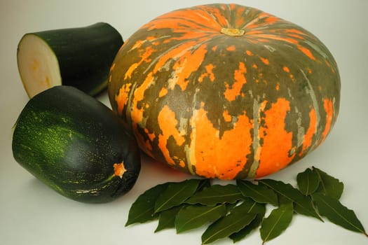 Ripe orange pumpkin and green ripe zucchini with a bay leaf on a white background. High quality photo