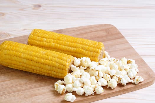 Boiled corn pob and sweet popcorn. Ears of cooked sweet corn on a wooden table scattered popcorn. High quality photoBoiled corn pob and sweet popcorn. Ears of cooked sweet corn on a wooden table scattered popcorn. Close-up, isolated.