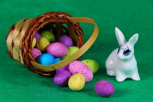White bunny with spilled colorful speckled egg basket on green
