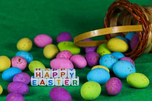 Happy Easter text beads and woven basket with colorful speckled eggs spilled on green