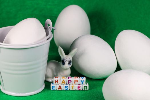 Happy Easter text beads and bunny with large white candy eggs and bucket on green