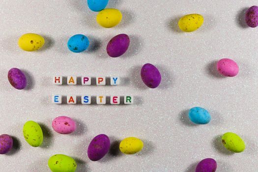 Happy Easter text beads with colorful speckled candy eggs on textured glitter background layout