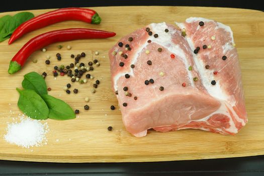 A piece of raw meat with pepper pods, peas and coarse salt on a wooden board.