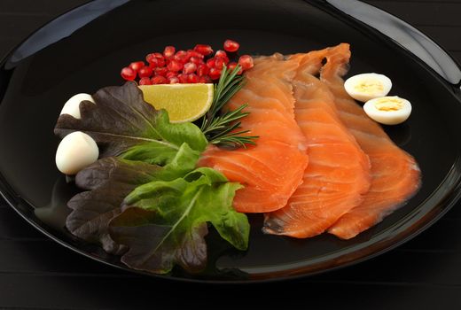 Salmon, sliced red fish with lime, rosemary and pomegranate seeds, served on a black background. Red fish. on a black platter with quail egg, lettuce and lemon. High quality photo