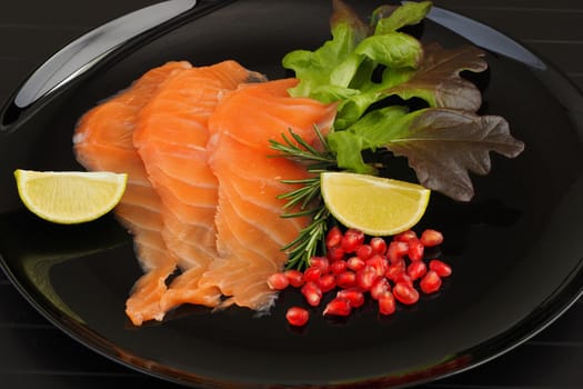 Salmon, sliced red fish with lime, rosemary and pomegranate seeds, served on a black background. High quality photo