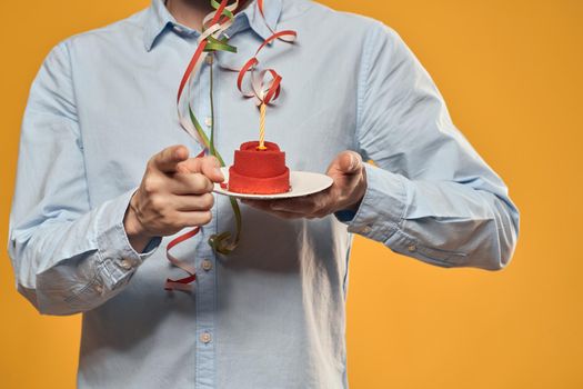 Guy with a cake in a plate on a yellow background holidays candle cropped view. High quality photo