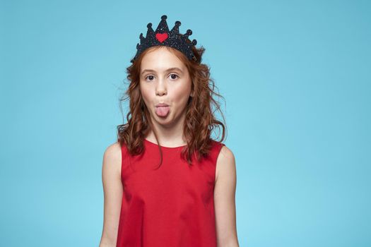 Girl with curly hair with a crown on her head red dress lifestyle blue background. High quality photo