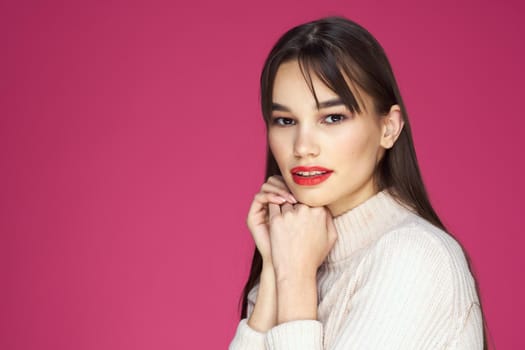 Brunette with long hair red lips cosmetics white sweater pink background cropped view. High quality photo