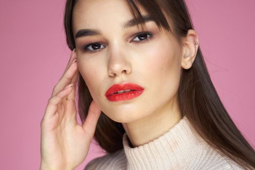 Brunette with long hair red lips cosmetics white sweater pink background cropped view. High quality photo