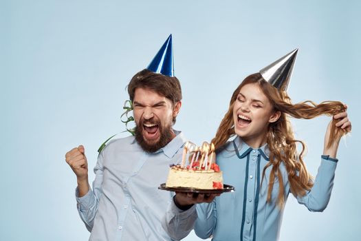 man and woman celebrate birthday with cake and in hats on blue background. High quality photo