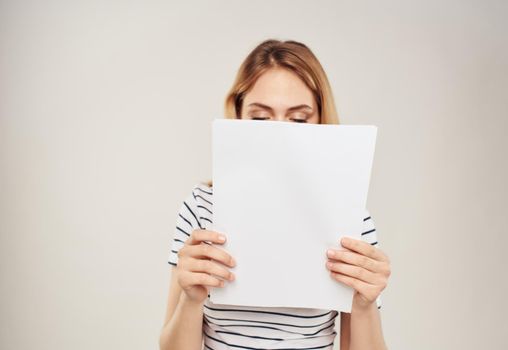 Woman in striped T-shirt blonde hair and a white sheet of paper on a beige background. High quality photo