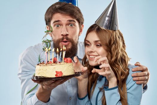 man and woman celebrate birthday with cake and in hats on blue background. High quality photo