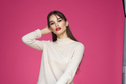 Brunette with long hair red lips cosmetics white sweater pink background cropped view. High quality photo