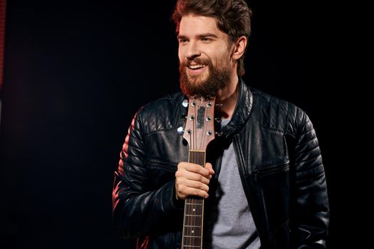 A man with a guitar in his hands leather jacket music performance rock star modern style dark background. High quality photo