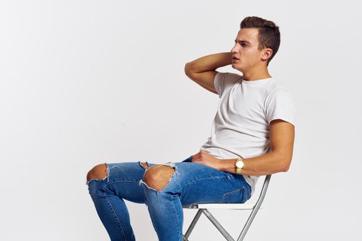 Man on a chair indoors torn jeans white t-shirt handsome face model light background. High quality photo