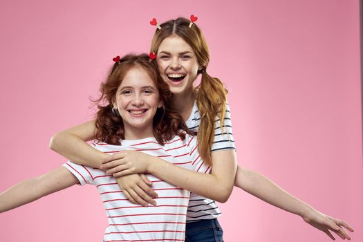 Happy sisters are having fun on a pink background and heart-shaped clothespins on their heads. High quality photo