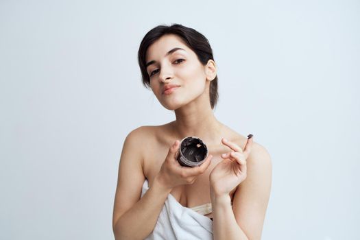 Pretty woman in white towel naked shoulders black cream in hands skin care spa procedure. High quality photo