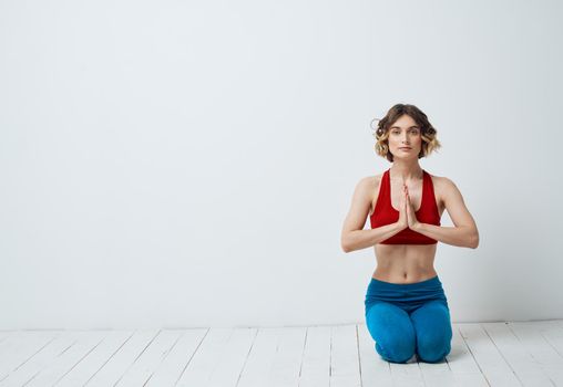 A woman sits on a light floor indoors with her hands joining yoga asanas for relaxation. High quality photo