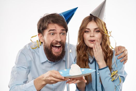 energetic man and woman with a cake and in hats celebrate a birthday on a light background. High quality photo