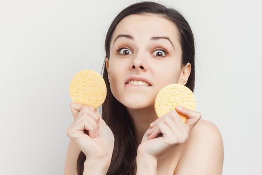 pretty brunette naked shoulders wipes her face but clean skin with a sponge. High quality photo
