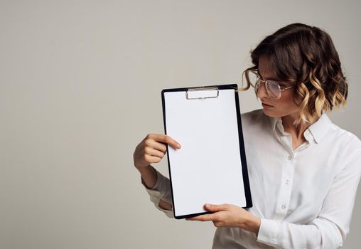 A woman is looking at a folder with a white sheet of paper on a gray mockup background. High quality photo