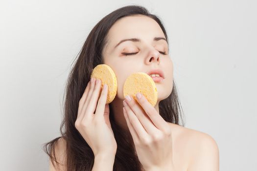 pretty brunette naked shoulders wipes her face but clean skin with a sponge. High quality photo